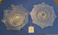 Top view of two etched glass crystal pieces laid on blue cloth, showing floral pattern and scalloped edges.