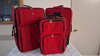 Front view of three red softshell suitcases showing two larger medium suitcases and one smaller carry-on suitcase, displaying their size and compartment design.