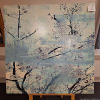 Photo of a square oil on canvas painting showing abstract leaves and branches in blue and black on light blue background.
