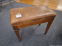 Front view of brown leather-like cushioned organ bench showing wear and scratches on wooden legs.