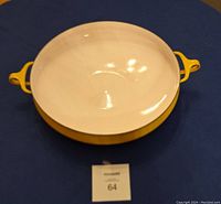 Yellow enameled paella pan on blue cloth, showing interior and one handle