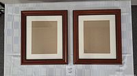 Two square brown wooden photo frames with off-white mats laid on white cloth surface.