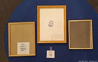 Three wooden photo frames arranged on blue fabric background; two have visible tags showing dimensions and one shows clear plastic glazing.