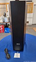 Front view of Axiom subwoofer speaker, showing black rectangular wooden cabinet with speaker grill and power cord on blue cloth