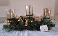 Clear view of the table centerpiece showing 3 gold glass candle holders with the pine and berry arrangement beneath.