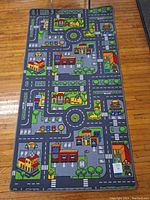 Top-down view of the full toy car road play mat on a wooden floor showing roads, roundabouts, parking spots, and buildings.