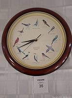 Full view of round wood framed clock with bird illustrations around the dial and black clock hands, showing 14 inch diameter.