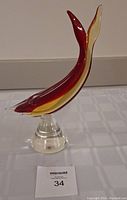 Single Murano glass whale figurine with red and yellow colors, mounted on a clear glass stand.