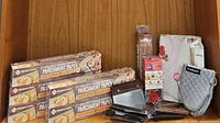 Assortment of baking tools including parchment paper boxes, metal spreaders, cookie cutter box, oven mitt, cutting board, and silicone mat