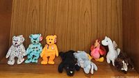 Nine assorted Beanie Babies plush toys displayed in a row against a wood panel background, showing various animals and colors, some with Ty heart tags visible.