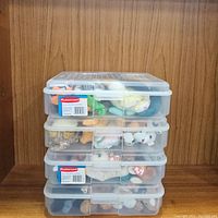 Four clear Rubbermaid containers stacked, filled with assorted Beanie Babies plush toys seen through the transparent lids