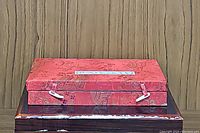 Photo of closed red brocade fabric calligraphy case with clasp fasteners on top of dark wooden box.