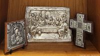 Group photo of three primary items: Last Supper metal relief, Virgin Mary & Jesus icon, and one decorative cross on a shelf.