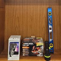 Photo showing all items: boxed Coleman lantern, Black & Decker Cyclone sander in box, handheld flashlight, blue level propped upright