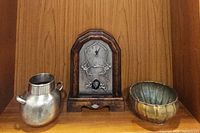 Photo showing all three items on a wooden shelf, including the tin-faced clock, pewter pitcher, and scalloped bowl.