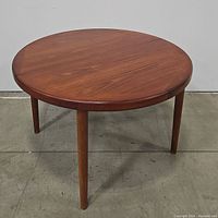 Front view of the round teak dining table showing the tabletop and legs.