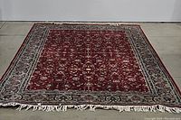 Full view of the red tufted rug showing its size and ornate pattern with a wide decorative border and fringed ends.