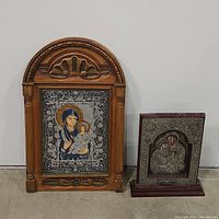 Photo showing both religious plaques, the Madonna plaque with carved wood frame and the Holy Family plaque with metal and wood base.