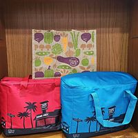 Front view of 3 reusable shopping bags including one vegetable print jute bag and two insulated cooler bags in red and blue with Trader Joe's storefront design.