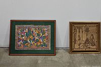 Two framed art pieces positioned upright on the floor against a wall, showing size and framing styles.