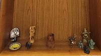 Photo of assorted small figurines and decorative items on wood background, including night light, trinket dish, carved floral piece, wooden bison and shepherd figurines.