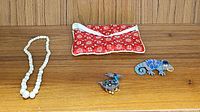 Overview photo of all four accessories: shell necklace, lizard pin, bird pin, and fabric clutch on wooden shelf