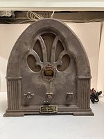 Front view of antique cathedral radio showcasing textured case, grille, control knobs, and badge.