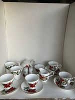 Full front view of the collection showing the teapot, sugar bowl, cups with saucers and creamer, all with red poinsettia and gold-rimmed designs.