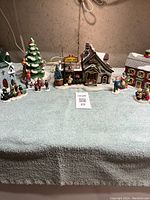 Full view of three ceramic lighted houses, a large decorated Christmas tree, and arranged holiday figurines.