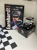 Photo showing Dale Earnhardt commemorative book, diecast golf cart model on its box, and portion of the checkered flag.