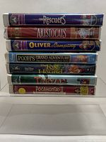 Side view showing stack of 7 Disney VHS movies including The Rescuers, The Aristocats, Oliver & Company, Pooh's Grand Adventure, The Fox and the Hound, Tarzan, Pocahontas II.