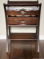 Front view of the walnut magazine rack showing its carved front panels and bottom shelf.