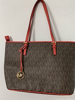 Front view of brown Michael Kors tote bag with MK logo print and red leather straps with gold-tone MK hanging charm