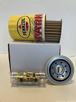 Photo showing the Pennzoil oil filter on its side exposing the filter element inside, signed branding visible, with the 1:64 diecast yellow Pennzoil stock car in a clear plastic case beside it