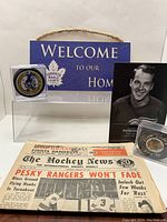 Lot showing signed Pierre Pilote puck in display case, Toronto Maple Leafs wooden welcome sign, Gordie Howe commemorative card/photo, signed Bob Errey puck in case, and The Hockey News newspaper from 1967