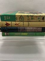 Side stack view showing the spine titles of four hardcover children's books including Habitat Elf, Pinocchio, Fantastic Voyage, When Debbie Danced