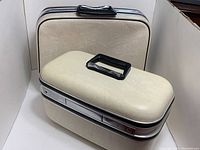 Large cream hard case suitcase and smaller matching makeup case with black handles and chrome details.