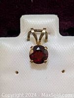 Front view of 10K gold pendant with round red garnet set in six-prong setting, placed on white textured stand.