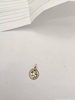 Photo of 10k gold pendant on a white background showing front view with rope-style design and inner letter element.