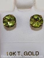 Close-up of the front of the earrings showing round faceted green peridot stones set in 10k gold.