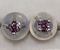 Front view showing two stud earrings with round purple stones in 14K white gold four-prong settings and clear silicone backs.