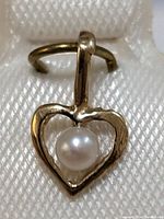 Close-up image of a 14K gold heart-shaped pendant with a centered white freshwater pearl, attached to a loop for chain threading.