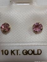 Close-up photo of two 10K gold earrings with round pink gemstones on display card marked 10 KT. GOLD.