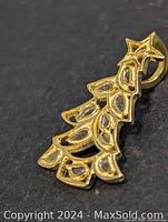 Close-up angled side view of gold-tone Christmas tree pendant with open leaf-shaped pattern and diamond accents.