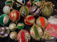 Overall view of vintage velvet and embroidered Christmas ornaments with gold cords on black background