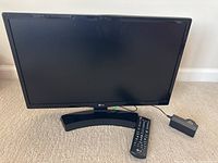 Front view of LG 22 inch television with stand and remote control placed on carpeted floor.