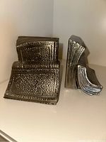 Front and side view of two bronzed metal bookends shaped like stacked books with textured detailing and bronzed finish