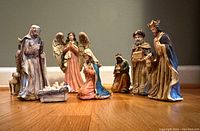 Front view showing all figurines lined up on hardwood floor including Baby Jesus, Mary, Joseph, Angel Gabriel, Shepherd, and Three Wise Men.