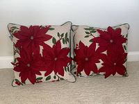 Pair of two square poinsettia pillows with red fabric flowers and green leaf prints on beige fabric