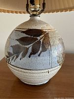 Close-up of pottery lamp base showing brown and tan leaf design on gray beige background.